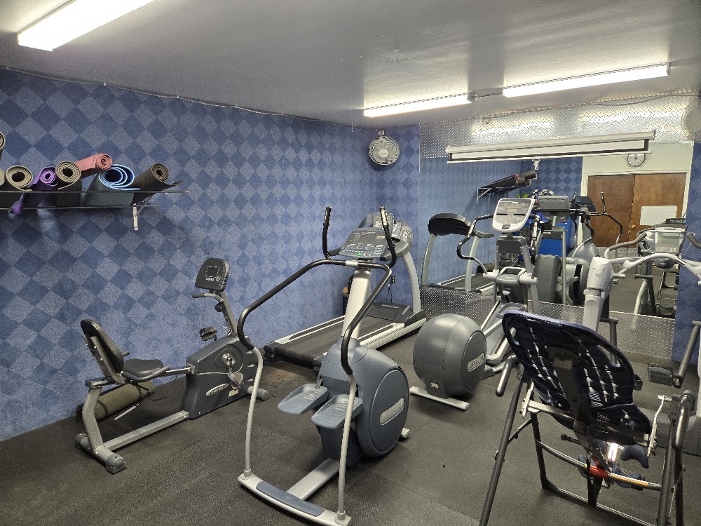 Small cardio room with multiple pieces of equipment and large mirror. 